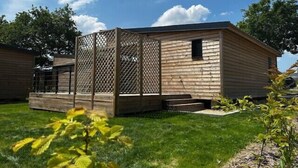 Una cabaña de madera con un enrejado, un pequeño porche y un patio cubierto de césped.