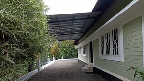 A covered outdoor area with a gravel path leading to a building with a green exterior and white trim. - 	“Your Family’s Perfect Getaway by the Riverside!” (Mankulam)