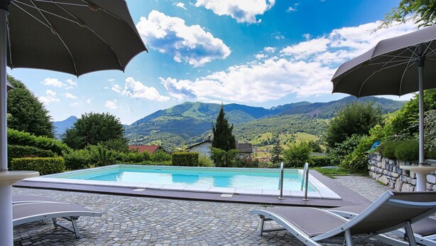 Uma piscina com espreguiçadeiras e guarda-sóis, rodeada por vegetação e montanhas.