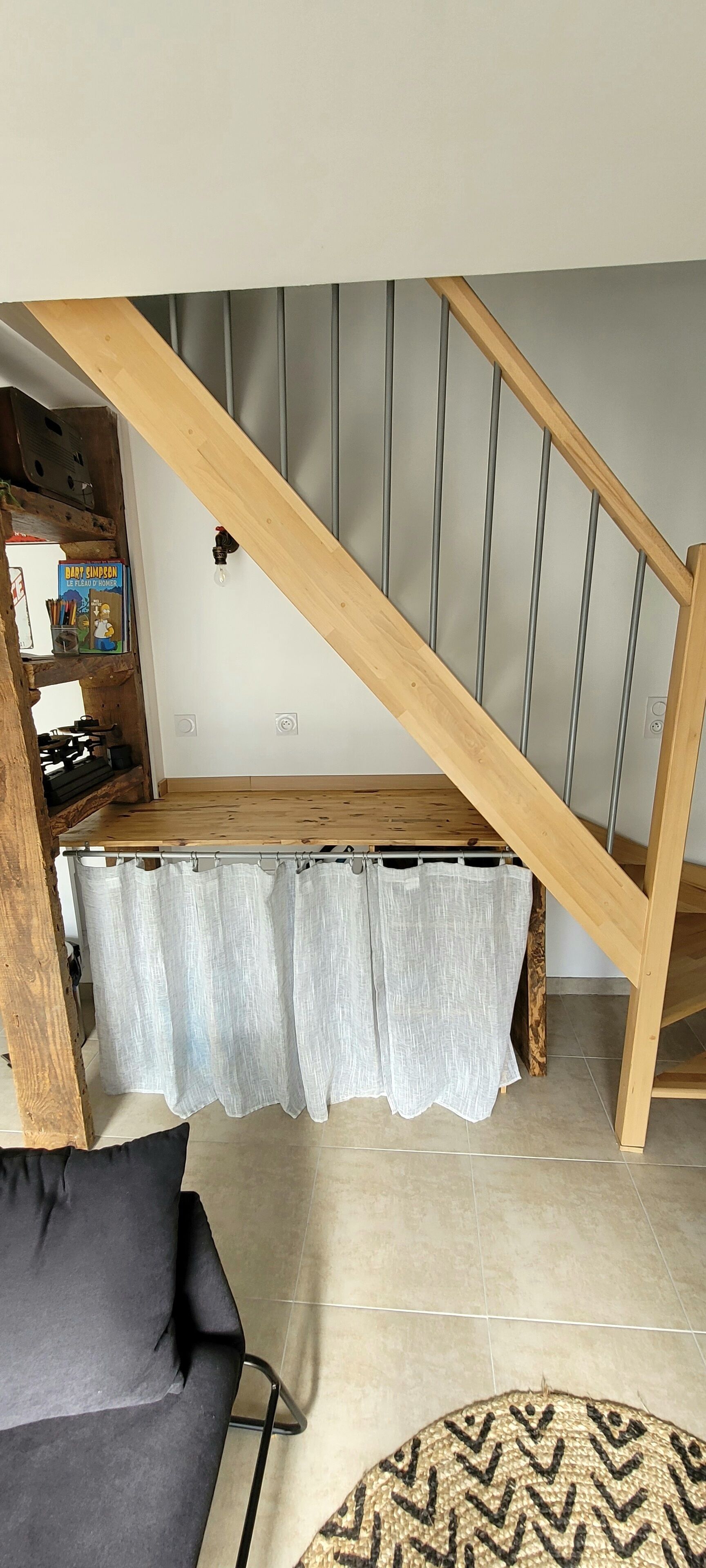 A loft bedroom with a wooden staircase, a bed under a window, and a desk area with a chair.