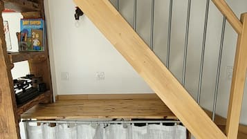 A loft bedroom with a wooden staircase, a bed under a window, and a desk area with a chair.