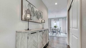 A hallway with a herringbone-patterned cabinet, a framed artwork above it, and a dining area in the background. - Rooftop Patio, Hot Tub, EV charging, Mtn views, close to AFA! (Palmer Lake)