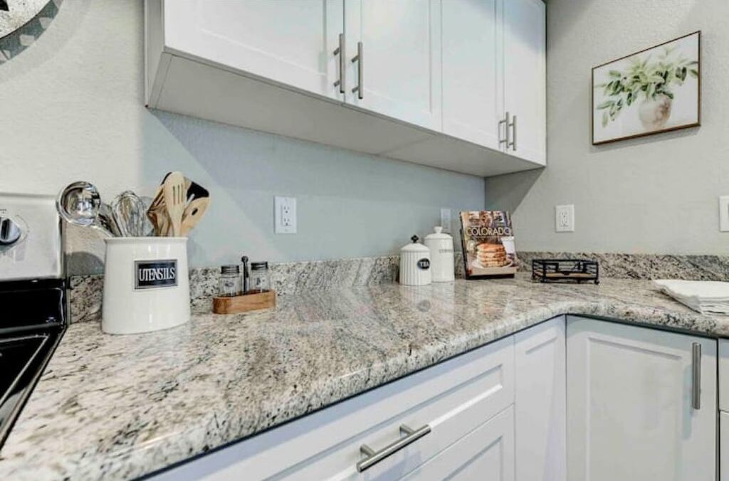 A kitchen with white cabinets, a granite countertop, and a coffee maker.