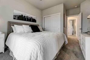 A bedroom with a large bed, a nightstand, a dresser, and a door leading to another room. - Rooftop Patio, Hot Tub, EV charging, Mtn views, close to AFA! (Palmer Lake)