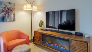 A living room with a flat-screen TV, a fireplace with a glass front, a sofa, a floor lamp, and a painting on the wall.