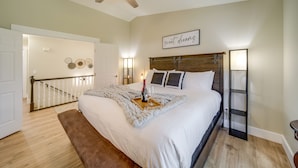 A bedroom with a large bed, a ceiling fan, a bedside table with a lamp, and a wall-mounted shelf.