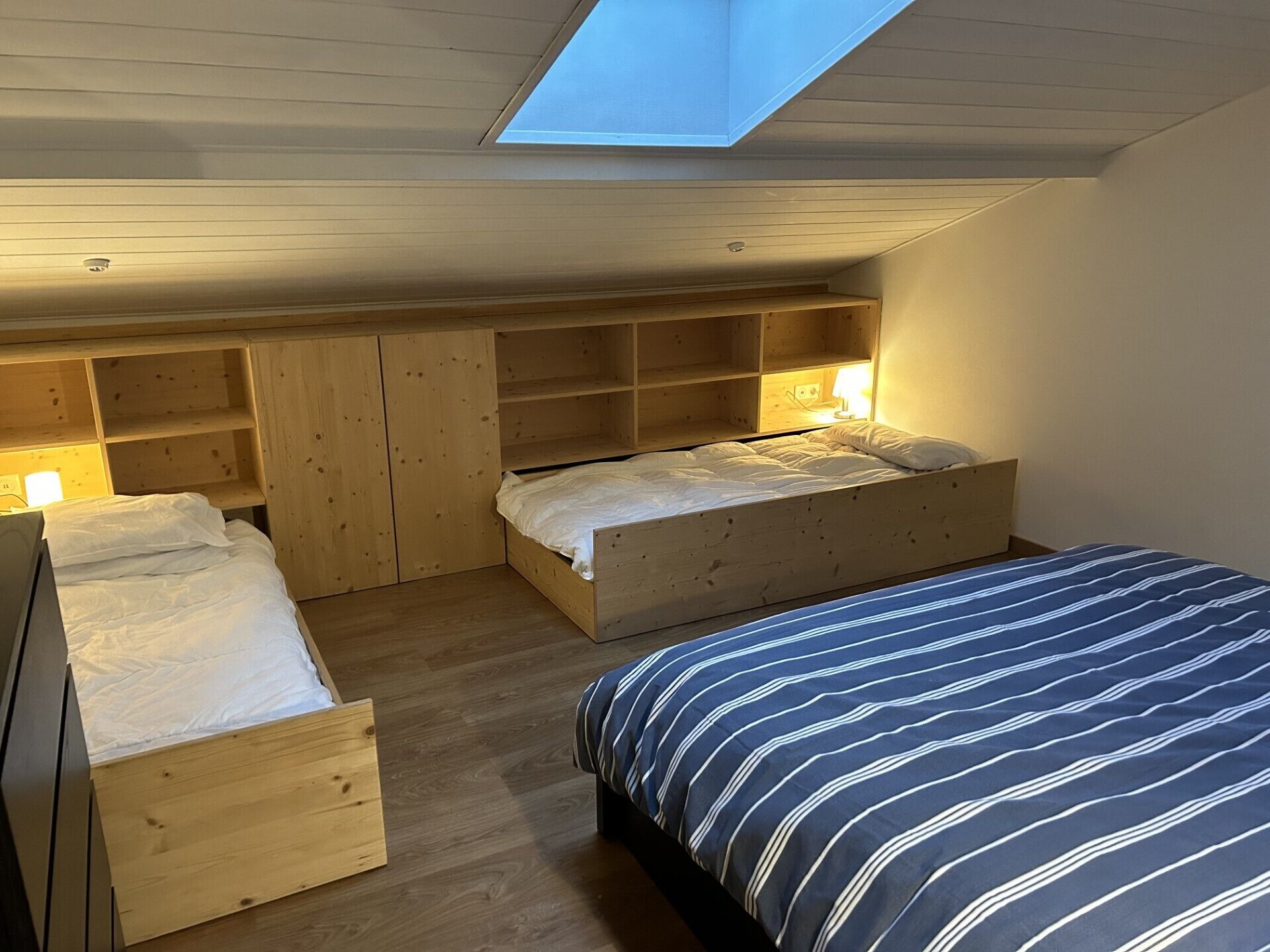 Un dormitorio pequeño con dos literas de madera, un tragaluz y estanterías empotradas.