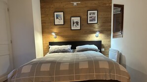 A neatly made bed with a checkered bedspread, two wall-mounted reading lamps, and framed pictures on the wooden wall behind the bed. - Walking distance of all lifts/town for summer and winter fun! Sleeps 9 (Morzine)