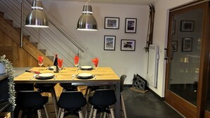 A dining area with a wooden table, black chairs, and pendant lights. There are framed pictures on the wall and a staircase in the background. - Walking distance of all lifts/town for summer and winter fun! Sleeps 9 (Morzine)