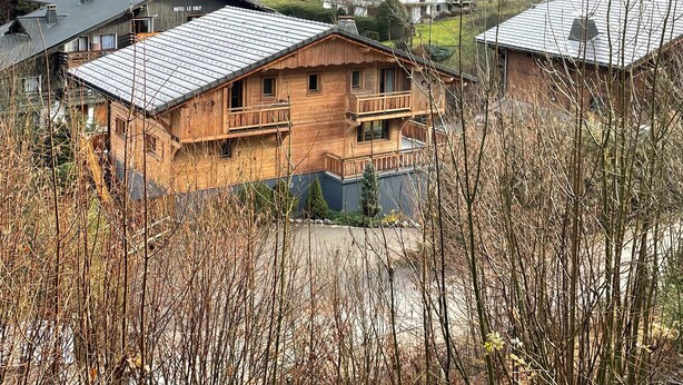 A cluster of wooden chalet-style buildings with balconies, set in a mountainous area with a view of a forested hill. - Walking distance of all lifts/town for summer and winter fun! Sleeps 9 (Morzine)