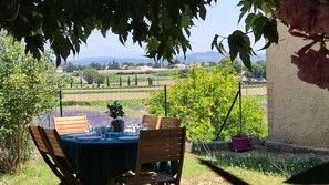 Ein Essbereich im Freien mit einem Tisch für zwei Personen, mit Blick auf einen Weinberg und die entfernten Hügel.