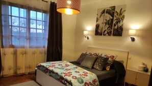 Quarto com cama, mesa de cabeceira, luminária e janela com cortinas.