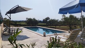 Piscina com espreguiçadeiras e guarda-sóis, cercada por vegetação e céu claro.
