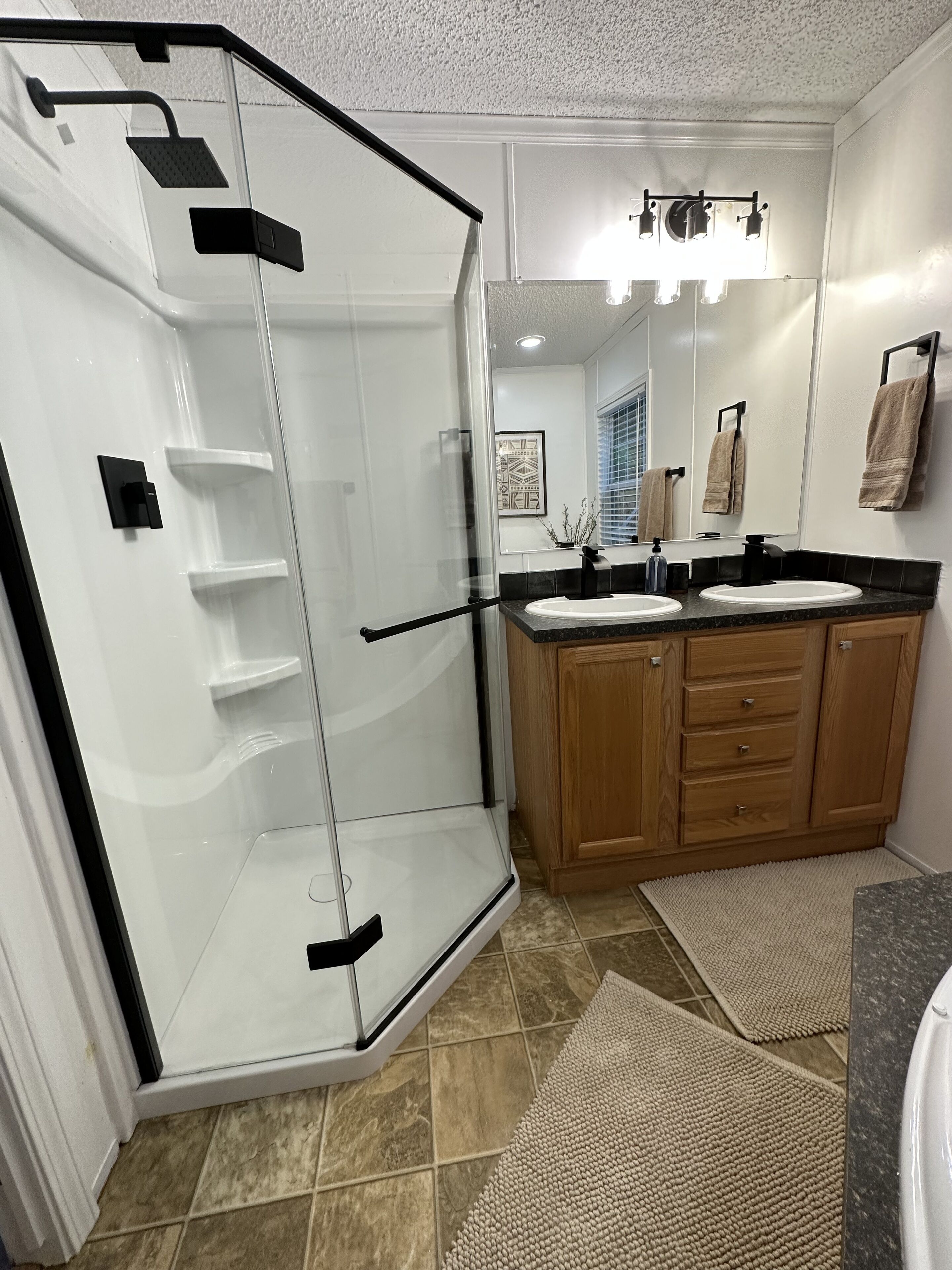 A modern bathroom with a glass shower enclosure, wooden cabinets, and a large mirror.