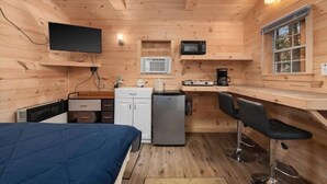 A compact wooden cabin with a bed, kitchenette, and a bar area.