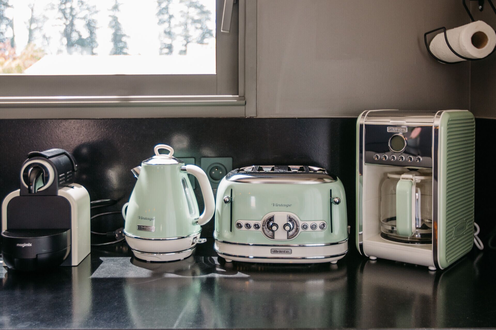 Eine Küche mit einem Toaster im Vintage-Design, einer Kaffeemaschine und einem Wasserkocher auf einer schwarzen Arbeitsplatte.