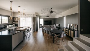 A modern kitchen with a central island, dining area with a large table, and a staircase leading to an upper level. - Villa Moka - private pool (Saumane-de-Vaucluse)