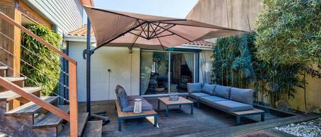 Un patio con una terraza de madera, mobiliario exterior y un paraguas grande.