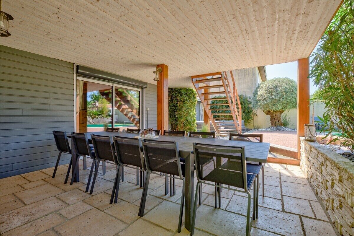 An outdoor patio with a dining table and chairs, a wooden staircase, and a view of the surrounding garden.