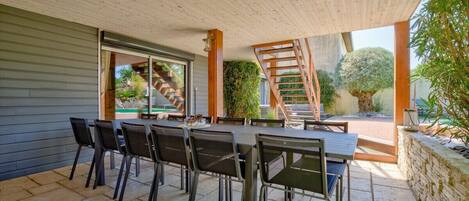An outdoor patio with a dining table and chairs, a wooden staircase, and a view of the surrounding garden.