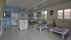 A spacious living area with a kitchen, dining table, and a sofa. There is a guitar and a radiator on the wall. - Charming family home- natural pool (Gujan-Mestras)