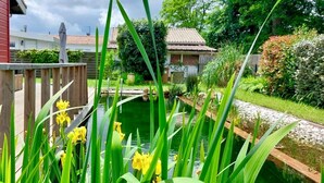 A garden with a pond, wooden fence, and houses in the background. - Charming family home- natural pool (Gujan-Mestras)