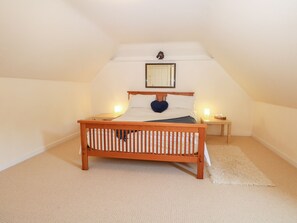 Quarto com cama de madeira, duas mesas de cabeceira, um criado-mudo, um tapete macio e um espelho na parede.