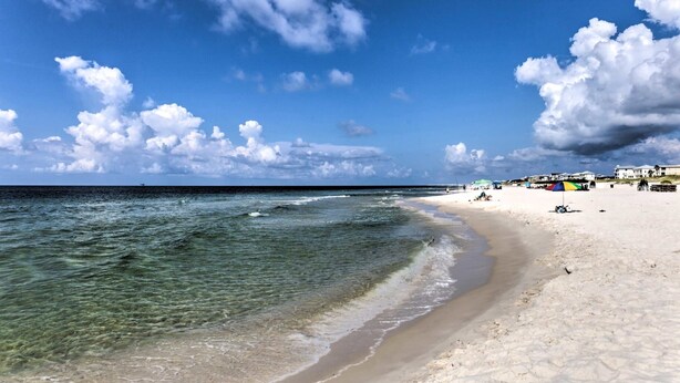 Una playa con agua cristalina, arena blanca y algunas sombrillas.