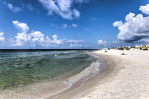 A beach with clear water, white sand, and a few umbrellas.