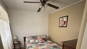 A small, single-bed room with a ceiling fan, a quilted bedspread, a bedside table with a lamp, and a framed picture on the wall. - Quiet Cottage located in the heart of Burr Oak State Park - #4 (Glouster)