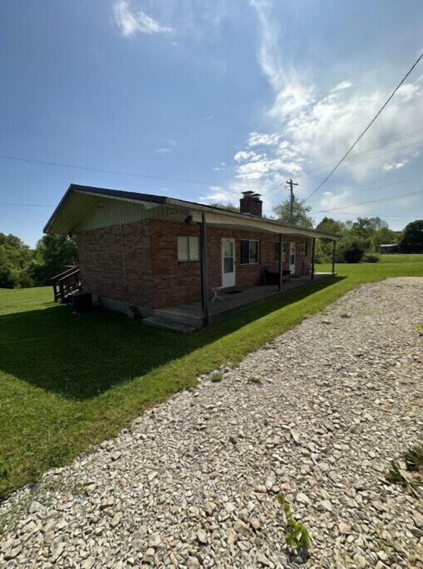 A small brick building with a porch, a gravel driveway, and a grassy lawn.