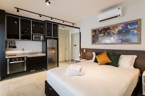 A modern hotel room with a large bed, a kitchen area, and a painting on the wall. - Studio Vitreo 66 (São Paulo)