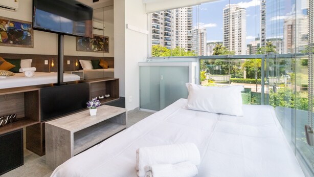 Ein modernes Hotelzimmer mit einem großen Bett, einem Fernseher und einem Balkon mit Blick auf die Stadt.