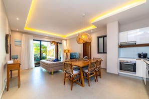 Een moderne woonkamer met een houten eettafel, een bank en een keuken met witte kasten en apparatuur.