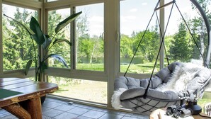 A room with a large window, a hanging chair, a table, and a plant. - Scenic Kettle River Cabin - Hike, Sauna, Kayaks & More-Your Next Retreat Awaits! (Willow River)