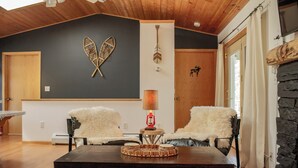 A cozy living room with a dark wall, wooden ceiling, and two plush chairs. A round wooden table with a decorative centerpiece is in the center. - Scenic Kettle River Cabin - Hike, Sauna, Kayaks & More-Your Next Retreat Awaits! (Willow River)