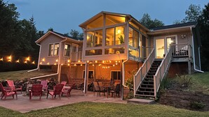 A two-story house with a balcony, outdoor seating area, and a staircase leading to the upper level. - Scenic Kettle River Cabin - Hike, Sauna, Kayaks & More-Your Next Retreat Awaits! (Willow River)
