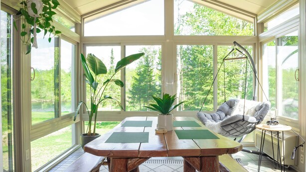 A conservatory with a wooden table, hanging chair, and potted plants. - Scenic Kettle River Cabin - Hike, Sauna, Kayaks & More-Your Next Retreat Awaits! (Willow River)