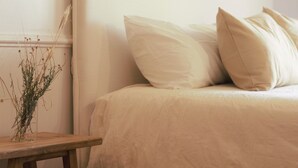 Ein Schlafzimmer mit einem Bett, Kissen und einem Nachttisch mit einer Vase getrockneter Pflanzen.