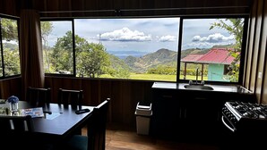 A kitchen with a large window overlooking a scenic landscape, a dining table with chairs, and a sink. - Campo Azul #3 - Monteverde (Provincia de Puntarenas)
