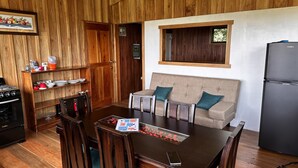 A compact kitchen with wooden walls, a dining table with chairs, a sofa with cushions, and a refrigerator. - Campo Azul #3 - Monteverde (Provincia de Puntarenas)