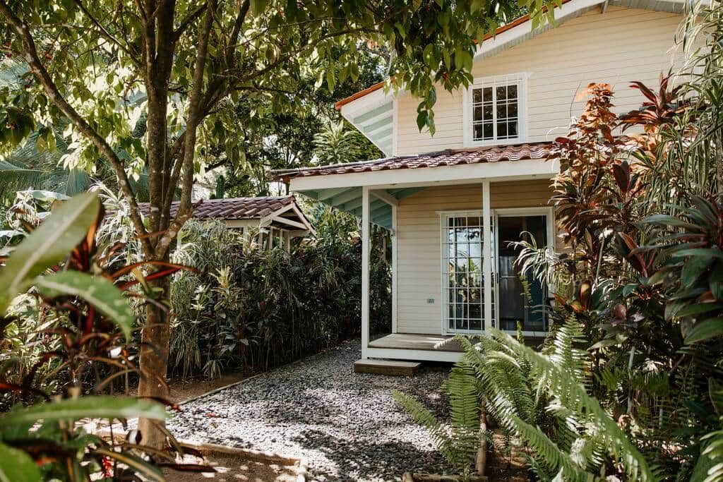 Une maison dotée d’un porche abrité, entourée d’une végétation tropicale luxuriante.