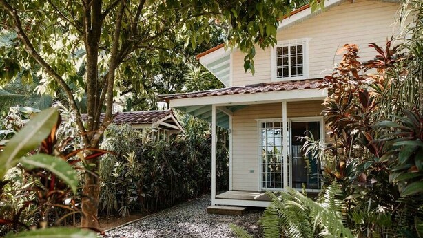 A house with a covered porch, surrounded by dense tropical vegetation.