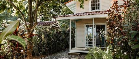A house with a covered porch, surrounded by dense tropical vegetation.