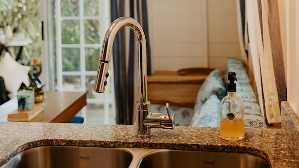A kitchen with a stainless steel sink, a bottle of dish soap, and a hanging light fixture.