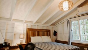 A bedroom with a wooden headboard, a bed with striped bedding, a nightstand with a lamp, and a window with curtains.