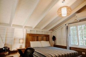 A bedroom with a wooden headboard, a bed with striped bedding, a nightstand with a lamp, and a window with curtains.