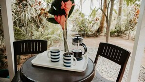 A round table with two chairs, a tray with two mugs, a coffee pot, and a flower.