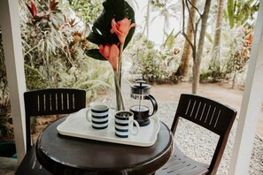 A round table with two chairs, a tray with two mugs, a coffee pot, and a flower.