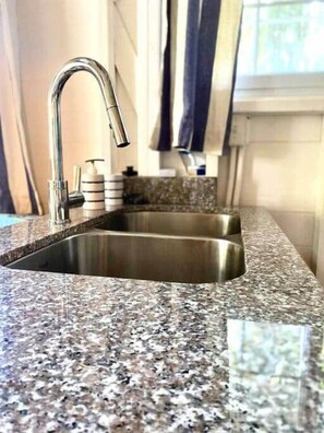 A kitchen with a granite countertop, stainless steel sink, and a window with curtains.